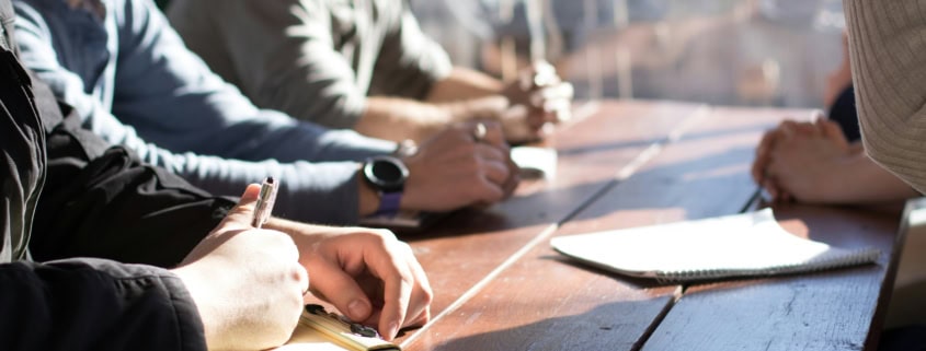 Personnes en réunion professionnelle prenant des notes pour retranscription
